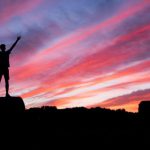Success - silhouette of man standing on high ground under red and blue skies