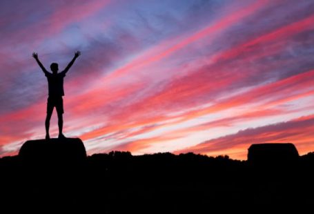 Success - silhouette of man standing on high ground under red and blue skies