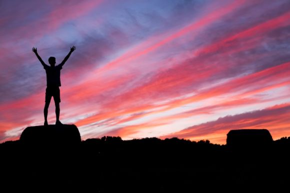 Success - silhouette of man standing on high ground under red and blue skies