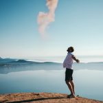 Happiness - man standing on sand while spreading arms beside calm body of water