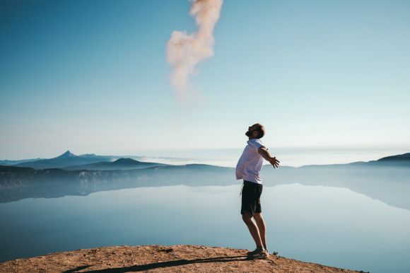 Happiness - man standing on sand while spreading arms beside calm body of water