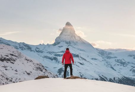 Success - person in red hoodie standing on snowy mountain during daytime