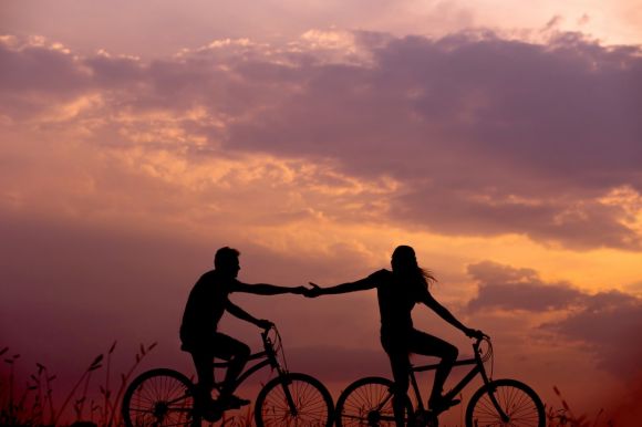 Relationship - woman on bike reaching for man's hand behind her also on bike